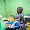 Sheilla skal også vaske op efter maden. Her drikker hun rent vand fra en pose imens. Man kan købe drikkevand i både flasker og poser i Ghana. Foto: Hans Bach.
